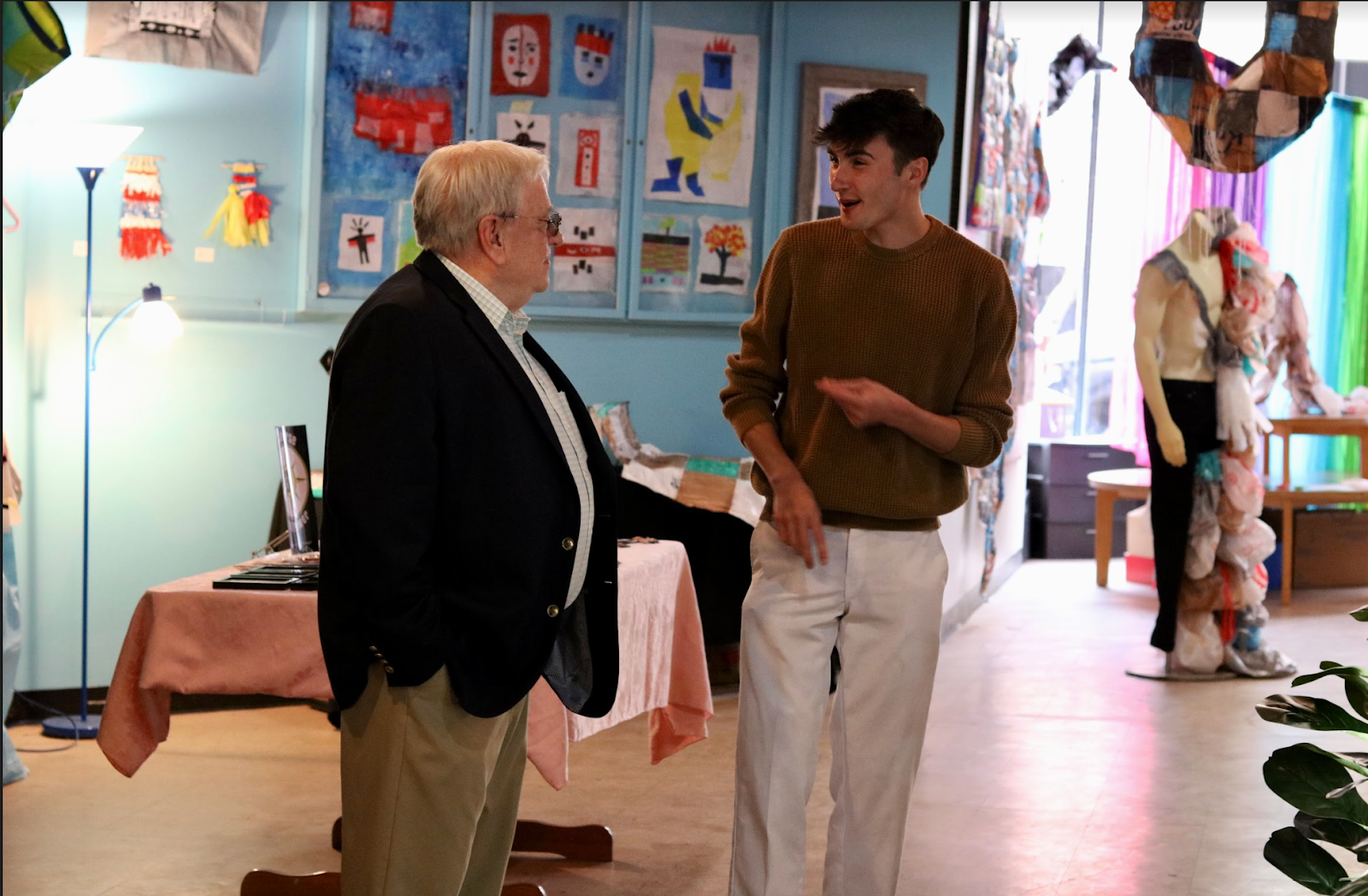 Man wearing a suit jacket talking to a man in a brown sweater