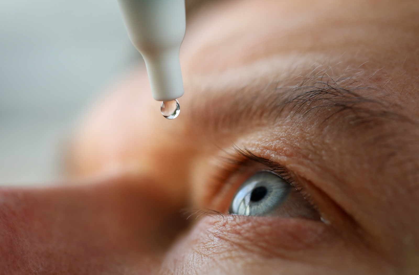 close up image of eye looking upwards, with an eye dropper with one drop of fluid held above