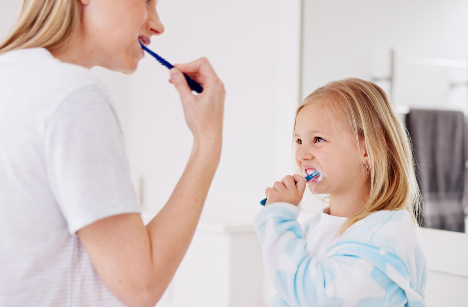 A mother teaching her young girl to brush her teeth in the bathroom.