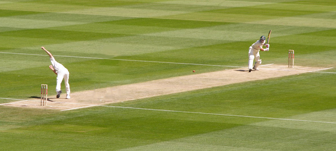 A bowler throws the ball towards a batter on a cricket pitch