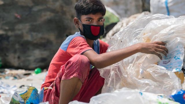 Хлопчик у масці для обличчя риється серед сміття в Бангладеш