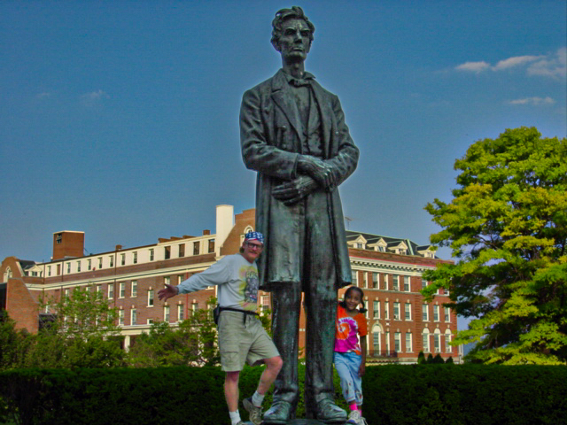 A statue of Abraham Lincoln with man holding Lincolns left leg and a young girl holds his right leg. 