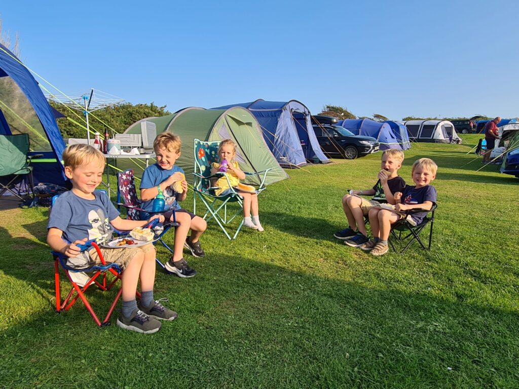 kids sitting on camping chairs on a campsite in the sunshine