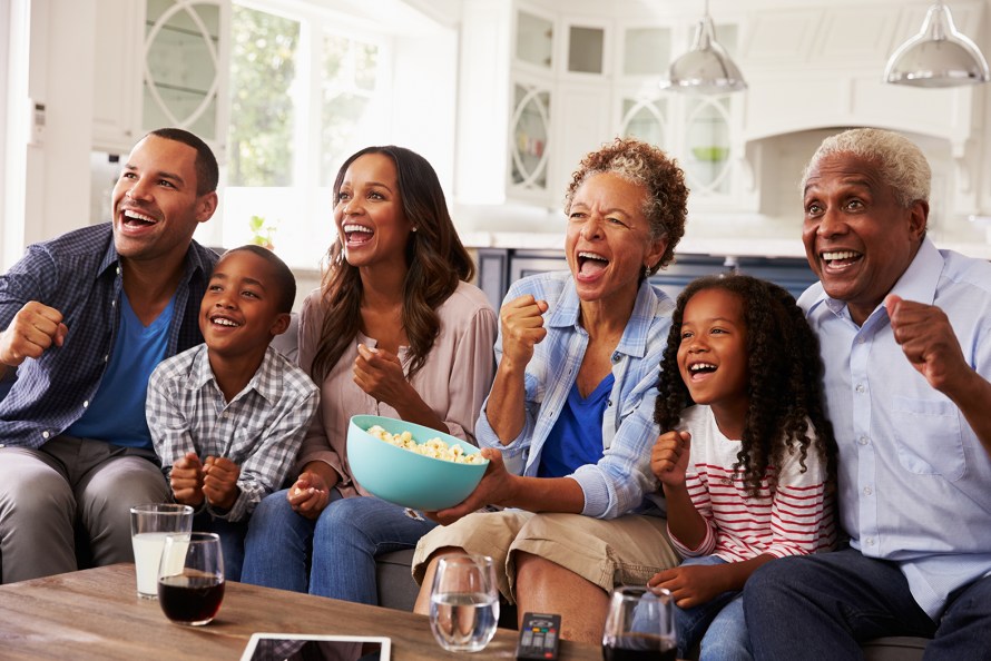 two kids, their parents, and grandparents watching television on a couch