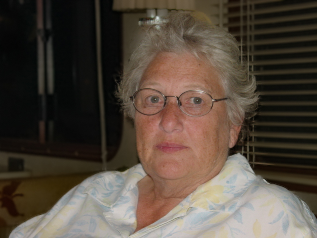 Woman with gray hair and glasses looks at the camera. 