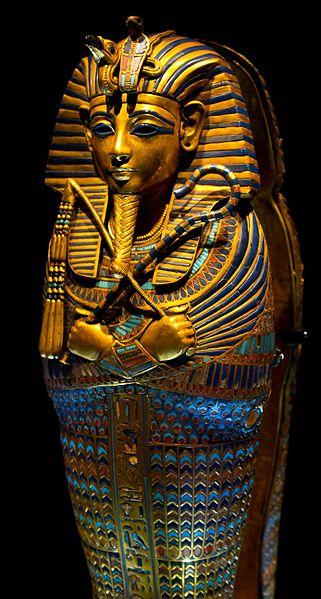 The golden and highly decorated sarcophagus of King Tut. The primary colors are gold and blue, and depicts a stylized images of the pharaoh with a ceremonial beard and holding two symbols.