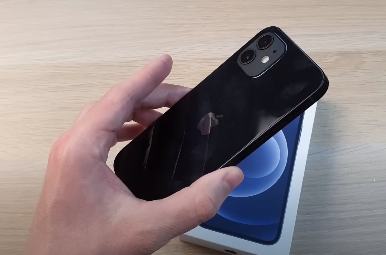 a hand holding the iPhone 12 with its package box in the background