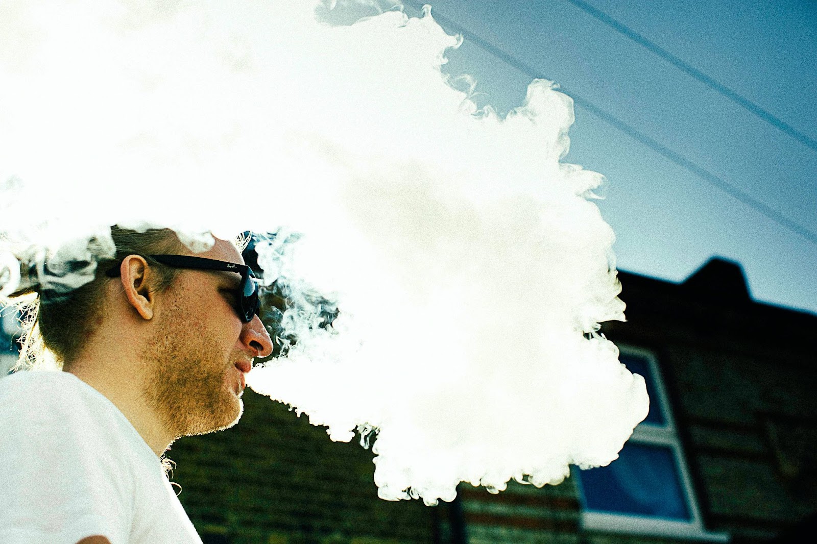 A man in sunglasses exhaling vape clouds