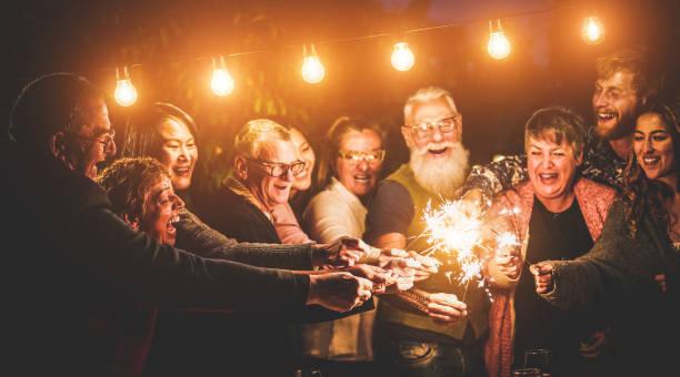 Happy family celebrating with sparkler fireworks on new year's eve - Different age of people having fun together in patio party - Celebration, winter and holidays concept - Focus on left hands Happy family celebrating with sparkler fireworks on new year's eve - Different age of people having fun together in patio party - Celebration, winter and holidays concept - Focus on left hands Elderly meeting new people stock pictures, royalty-free photos & images