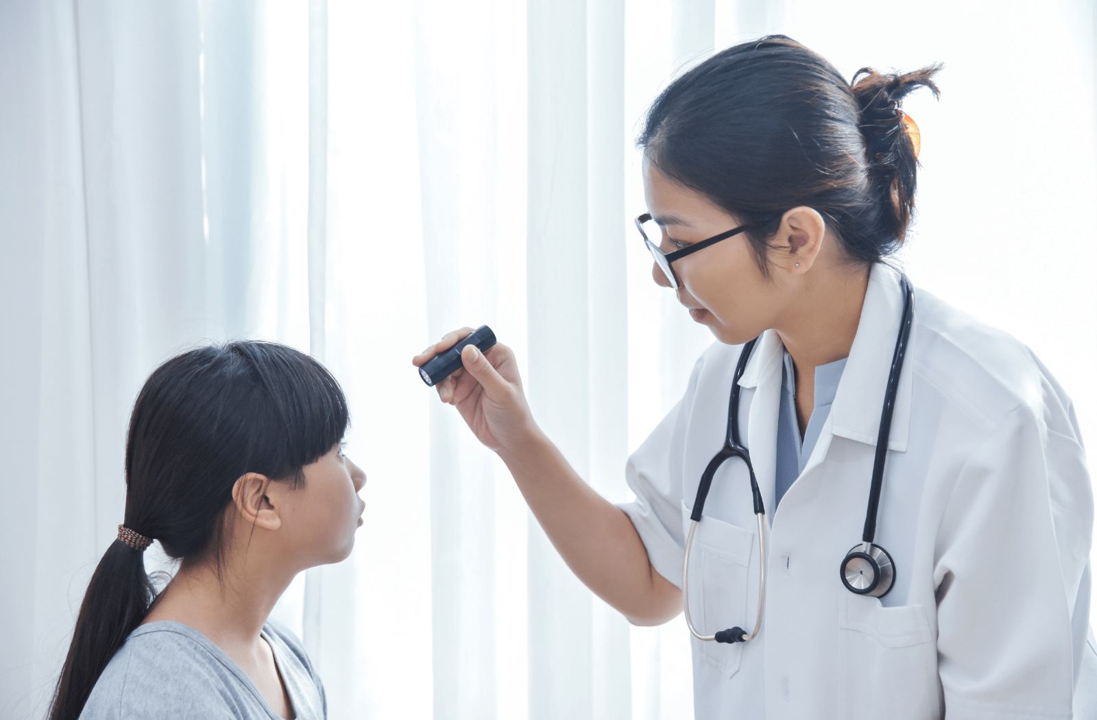A female optometrist using a light to look into a young girl's eyes