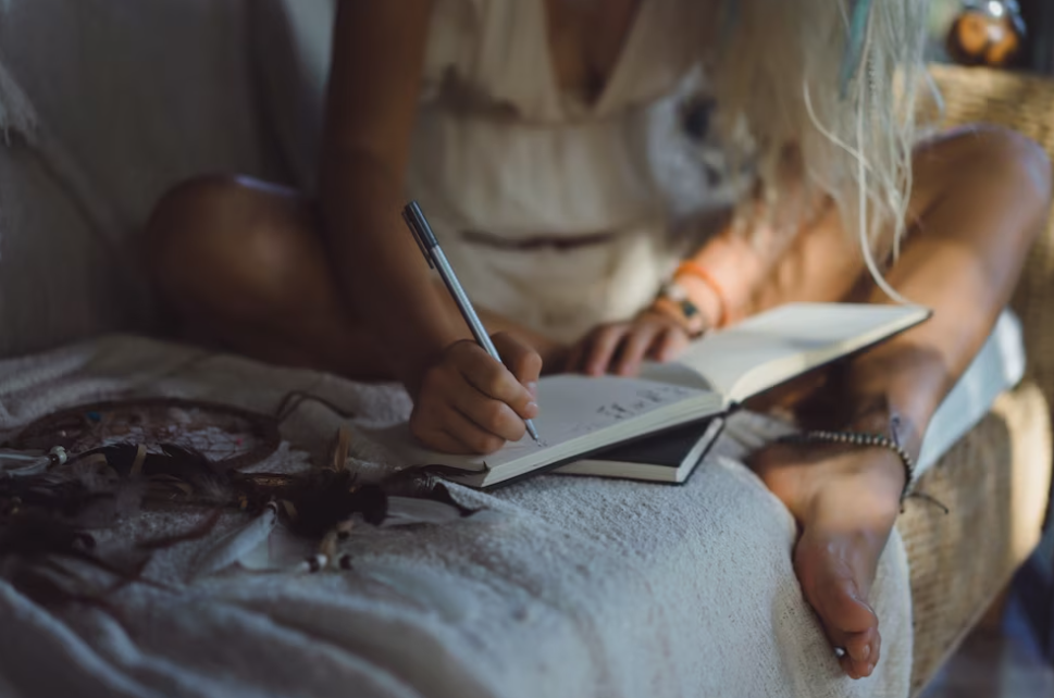 girl in a white dress makes notes in her notebook sitting on the bed
