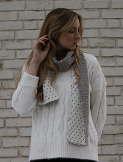 woman wearing a white and gray reversible scarf in front of a brick wall