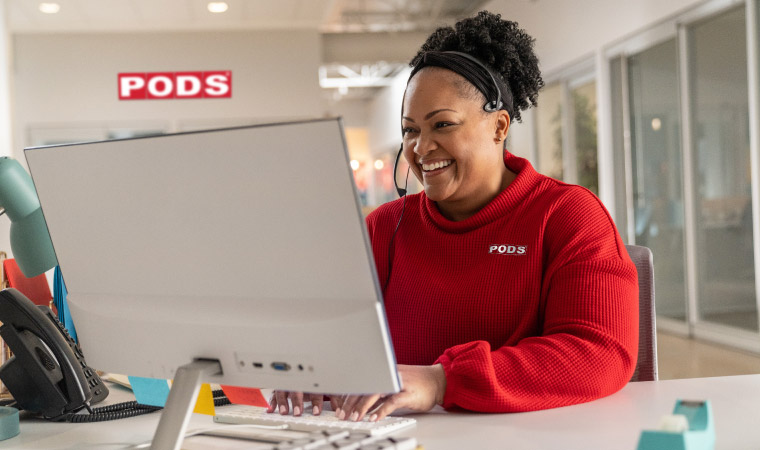 Penny, a PODS customer service rep, sits at her desktop while cheerfully helping a customer over the phone.