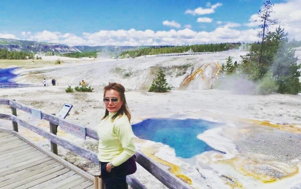 Image of Candy standing on a boardwalk with the hot springs of Yellowstone National Park in the background