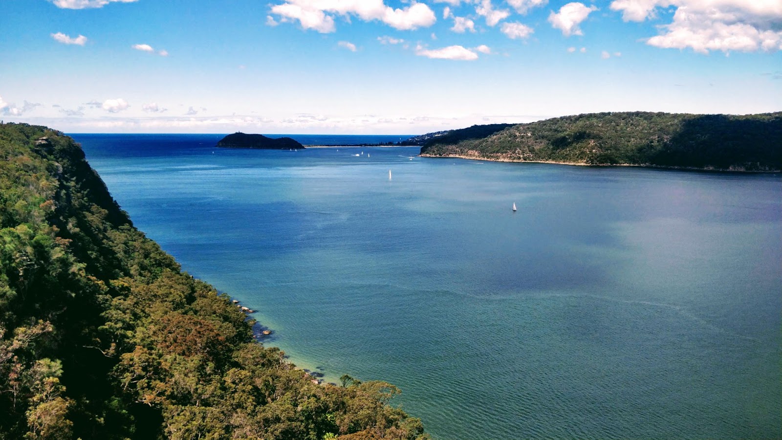 View from lookout across water towards ocean and land on other side of river with sailboats.