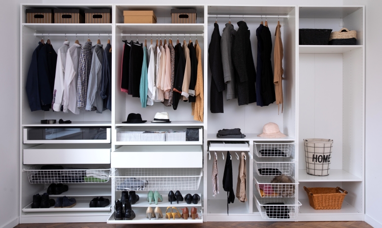 A closet shelf holds clothes, hates, and shoes. Each article is organized by its color.