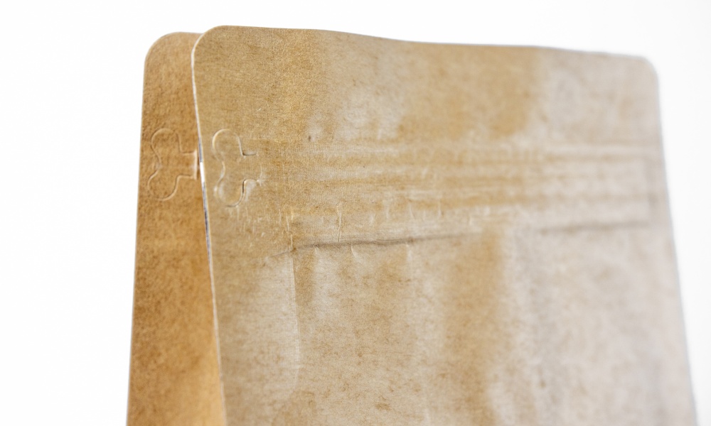 Close up of the top of an unbleached kraft paper coffee pouch, closed, highlighting the resealable zipper. 