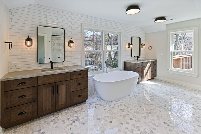floor-to-ceiling-tiled-bathroom-with-white-subway-tile-walls-two-natural-stained-cabinet-vanities-matte-black-harware-and-a-soaker-tub-under-a-picture-window