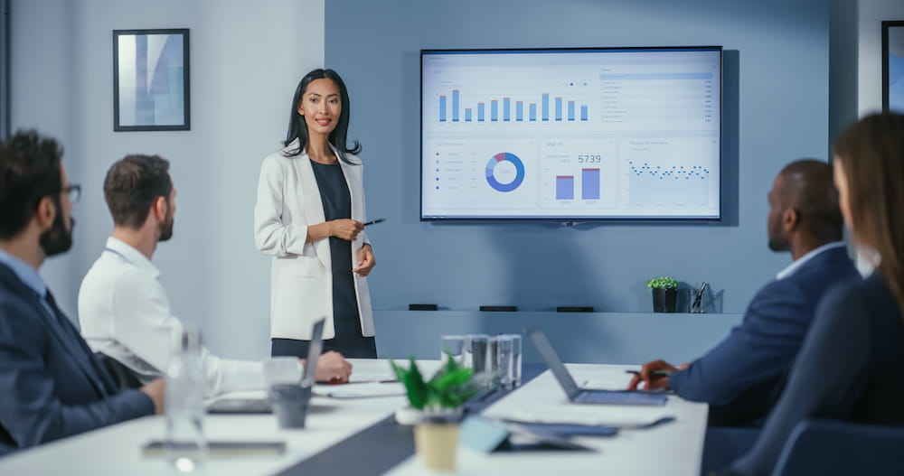 Female employee showing business analytics through data visualization to coworkers in conference room