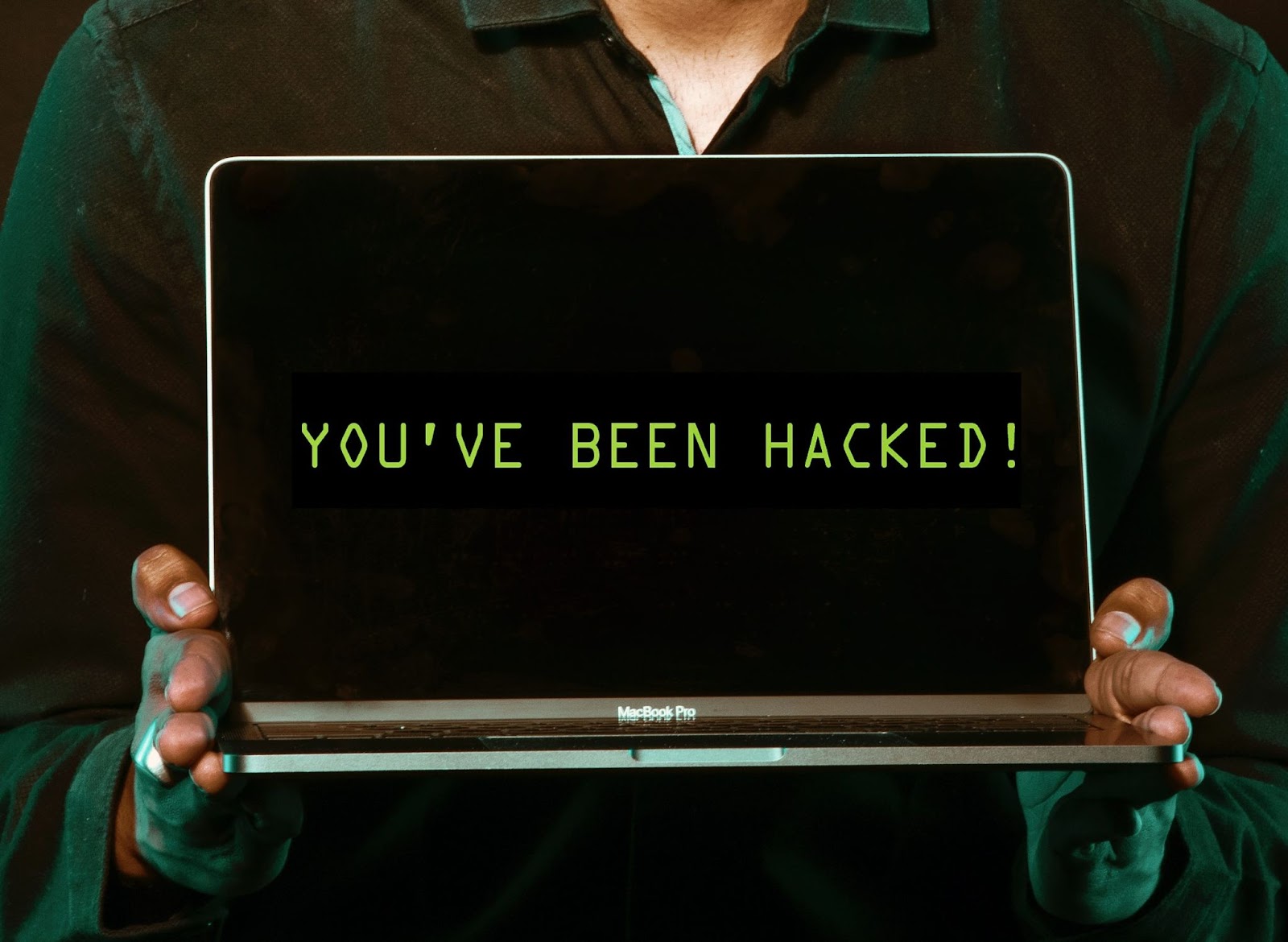 A man holding a laptop, with the laptop screen saying "You've been hacked".