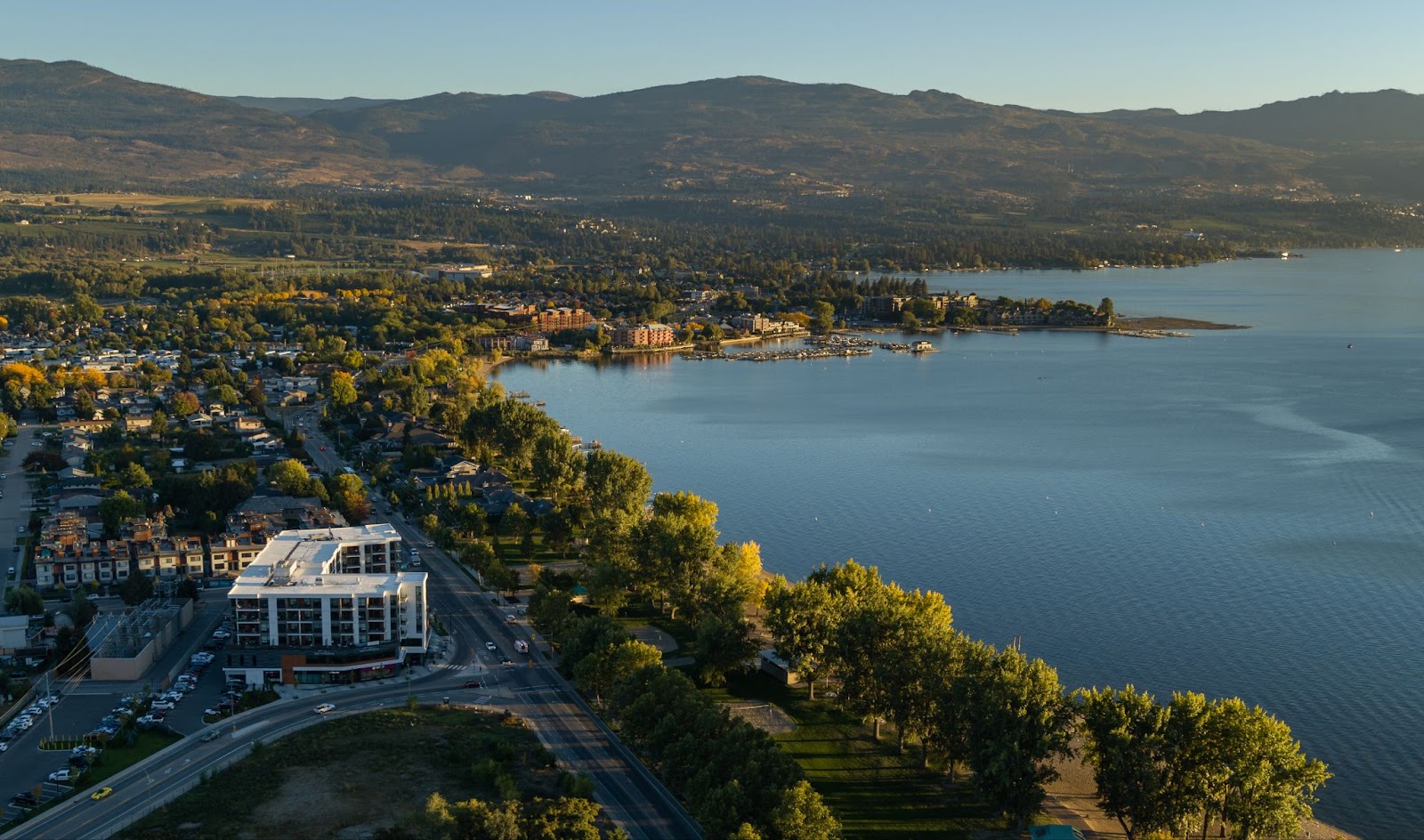 a birds-eye view of The Shore Kelowna, with the lake, Gyro beach and valley mountains in the distance.