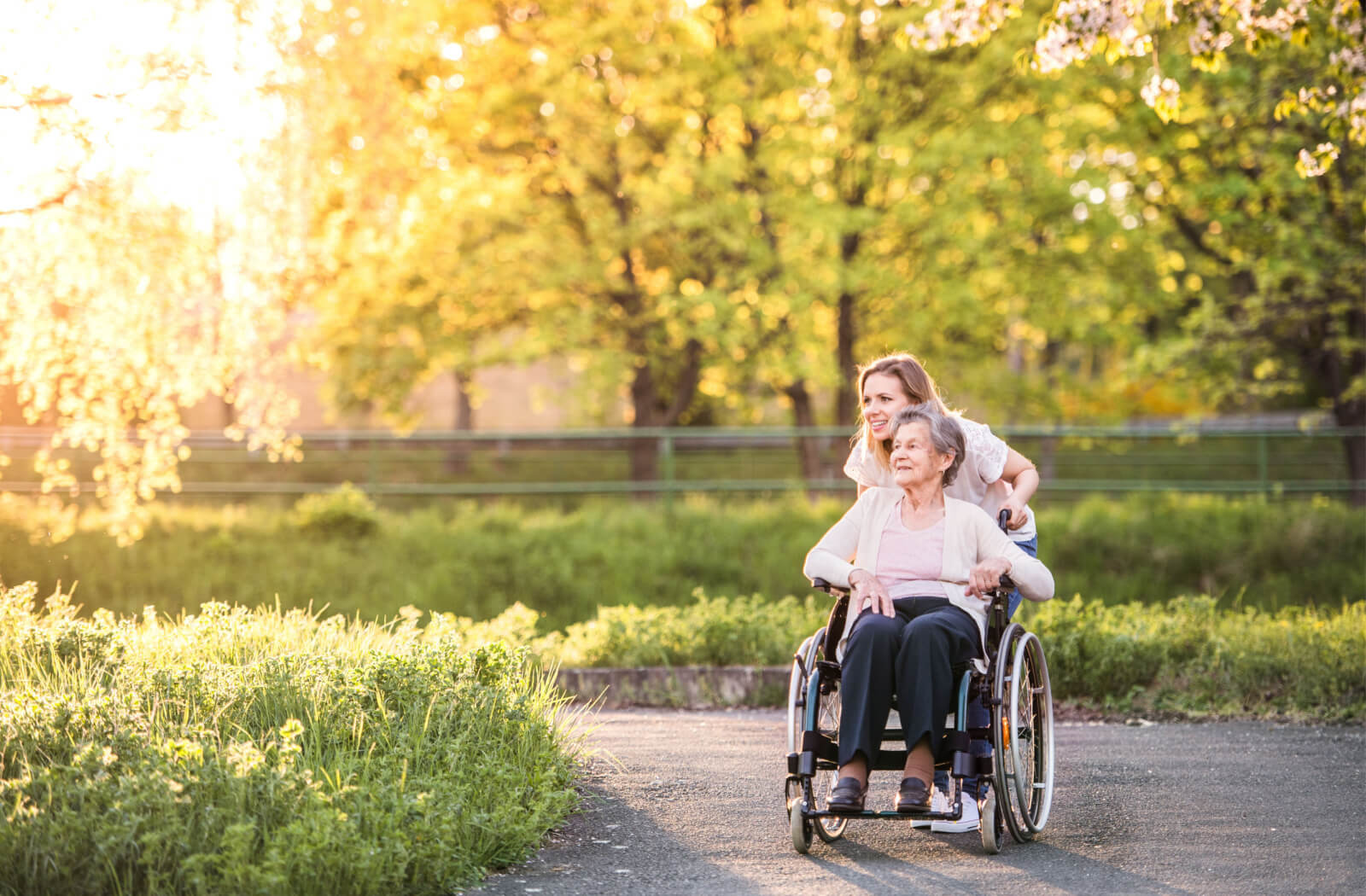 A young woman helping her mother in a wheelchair while having a nice time outside in a park.
