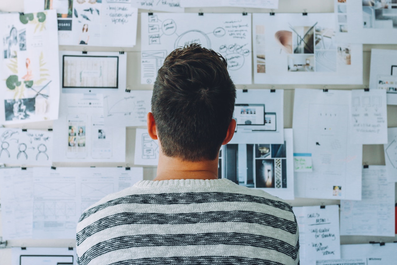 man wearing black and white striped shirt looking at white printer papers on the wall