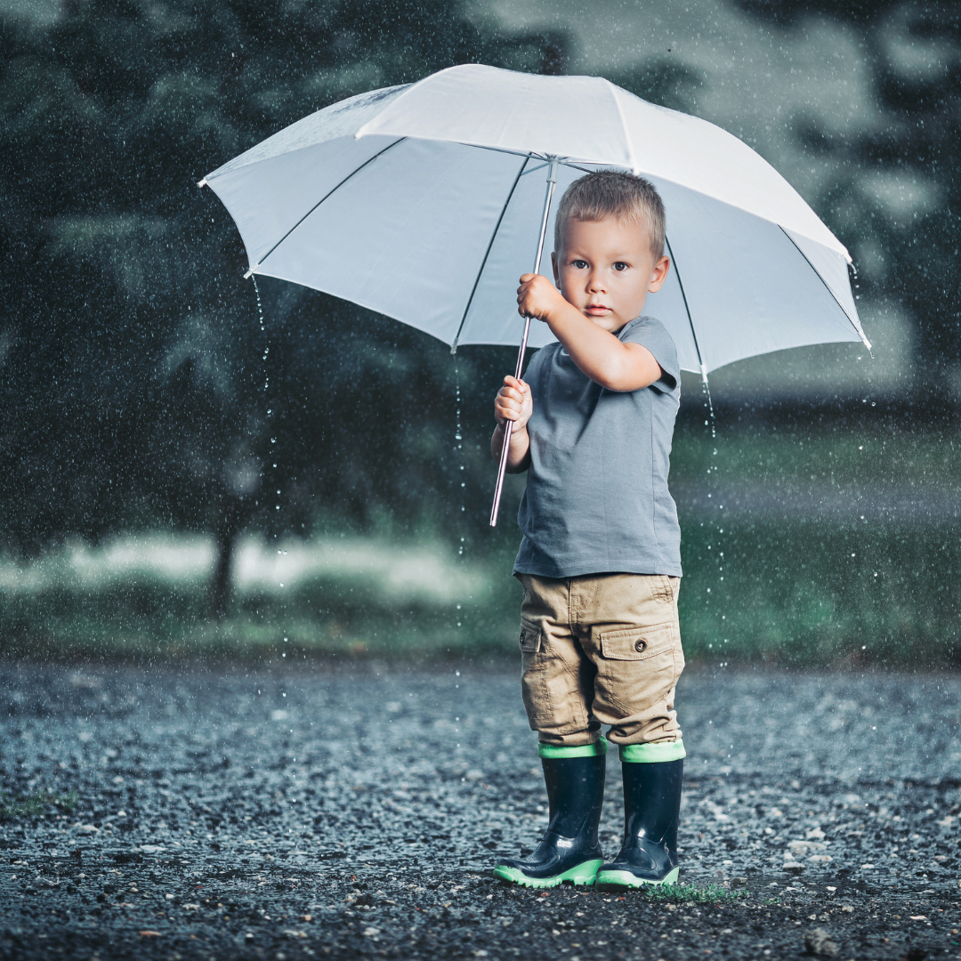 Toddler carrying an umbrella under the rain