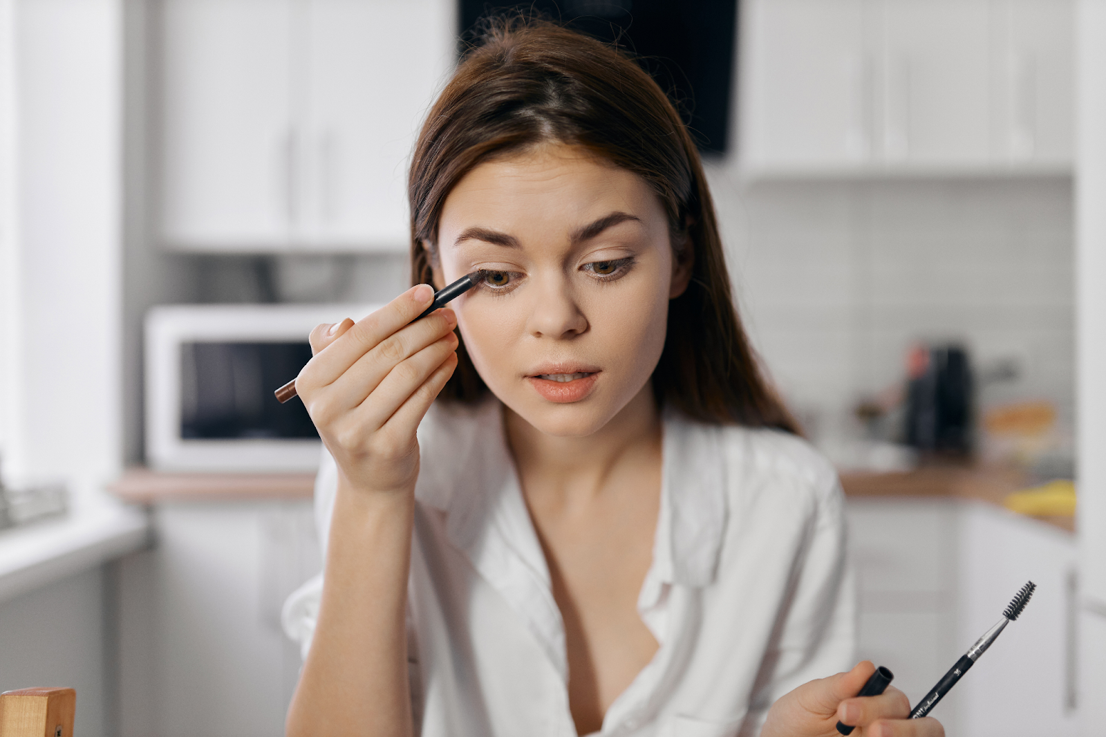 mulher em sua cozinha desenhando um delineado em seus olhos