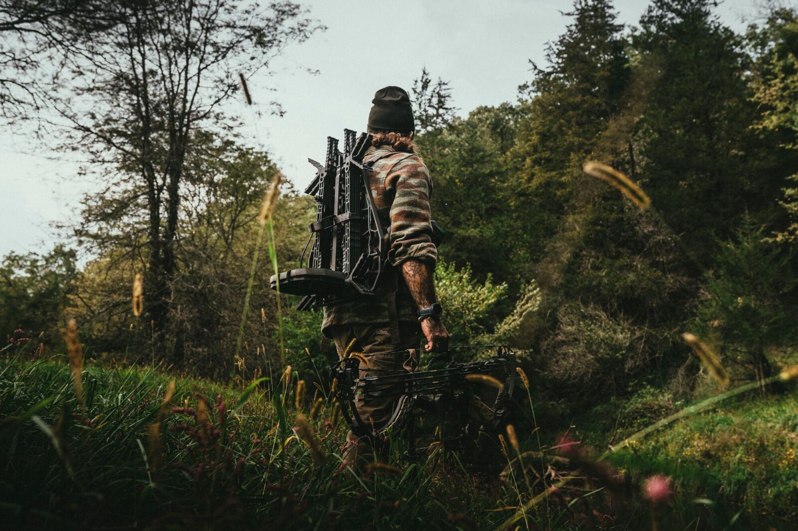 A bowhunter stands in the woods with a Lone Wolf treestand pack on his back. 