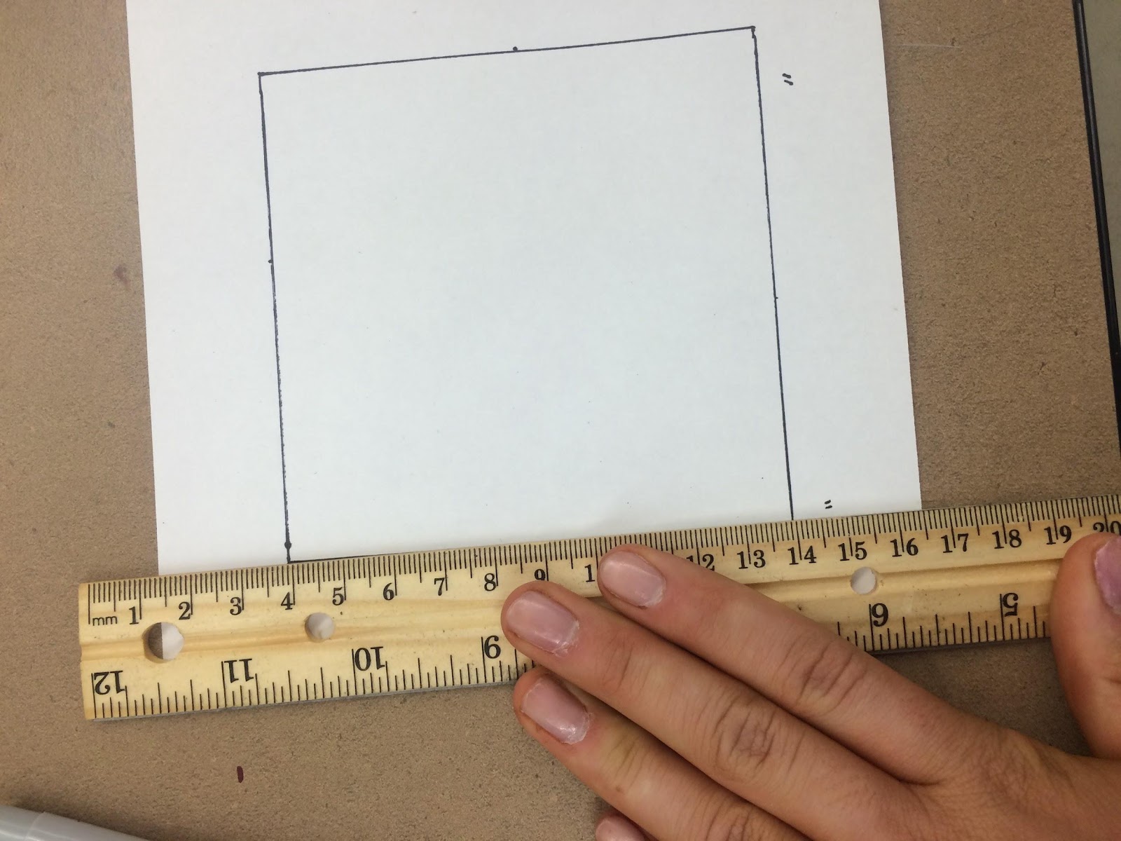 Picture of hand holding a ruler and measuring a piece of paper.