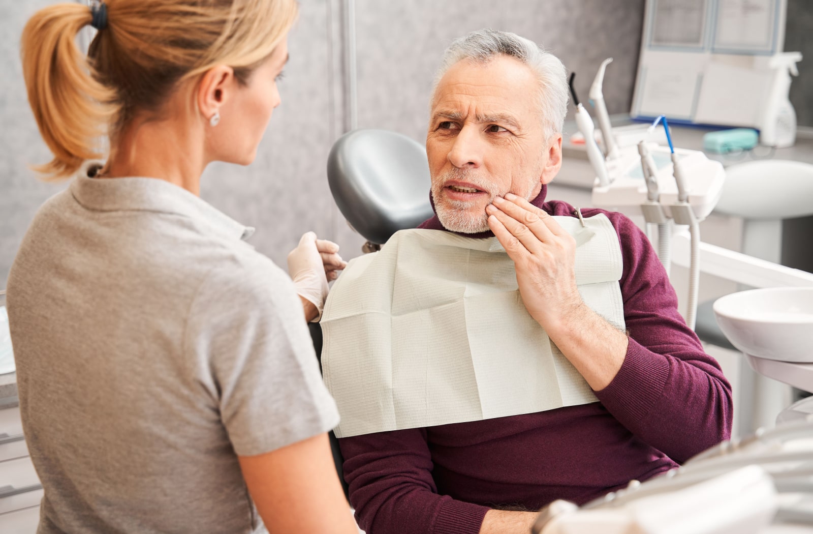 A man discusses his tooth pain with a dental hygienist at his dentist office.