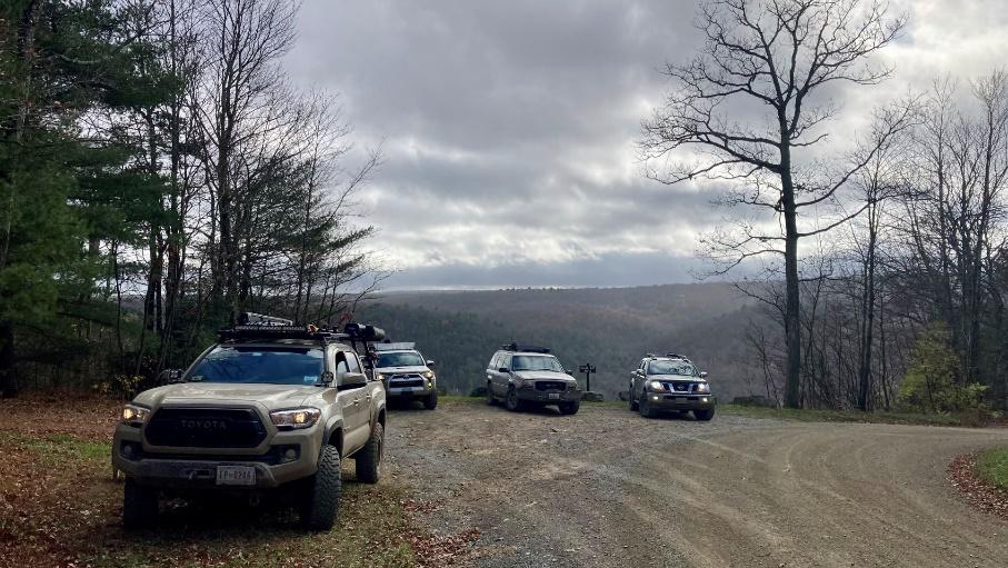 A group of cars parked on a dirt road with trees on either side

Description automatically generated with medium confidence