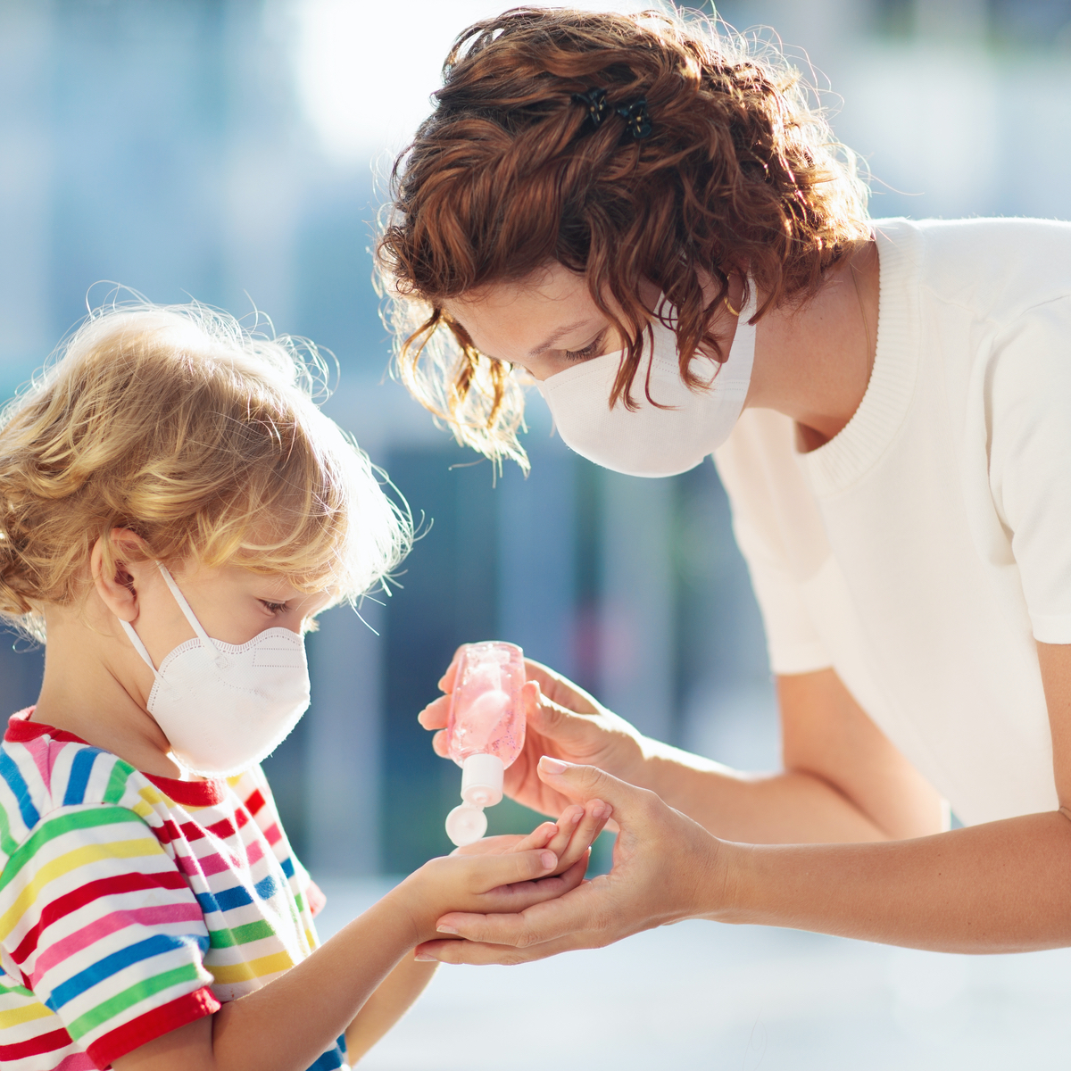 Masked mother applying hand sanitizer to masked young child.