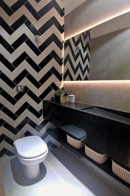 Banheiro com revestimentos trabalhos na parede em zig zag preto e branco, pia de granito preto e espelho retangular com led de fundo.