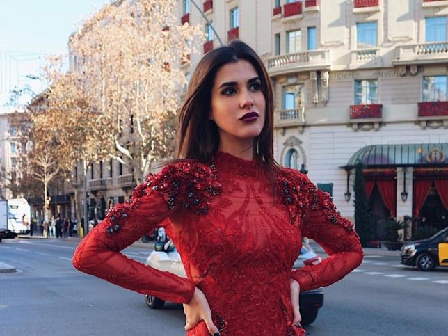 La influencer de estilo María Turiel posa en la calle con un vestido rojo, mirando a la lejanía