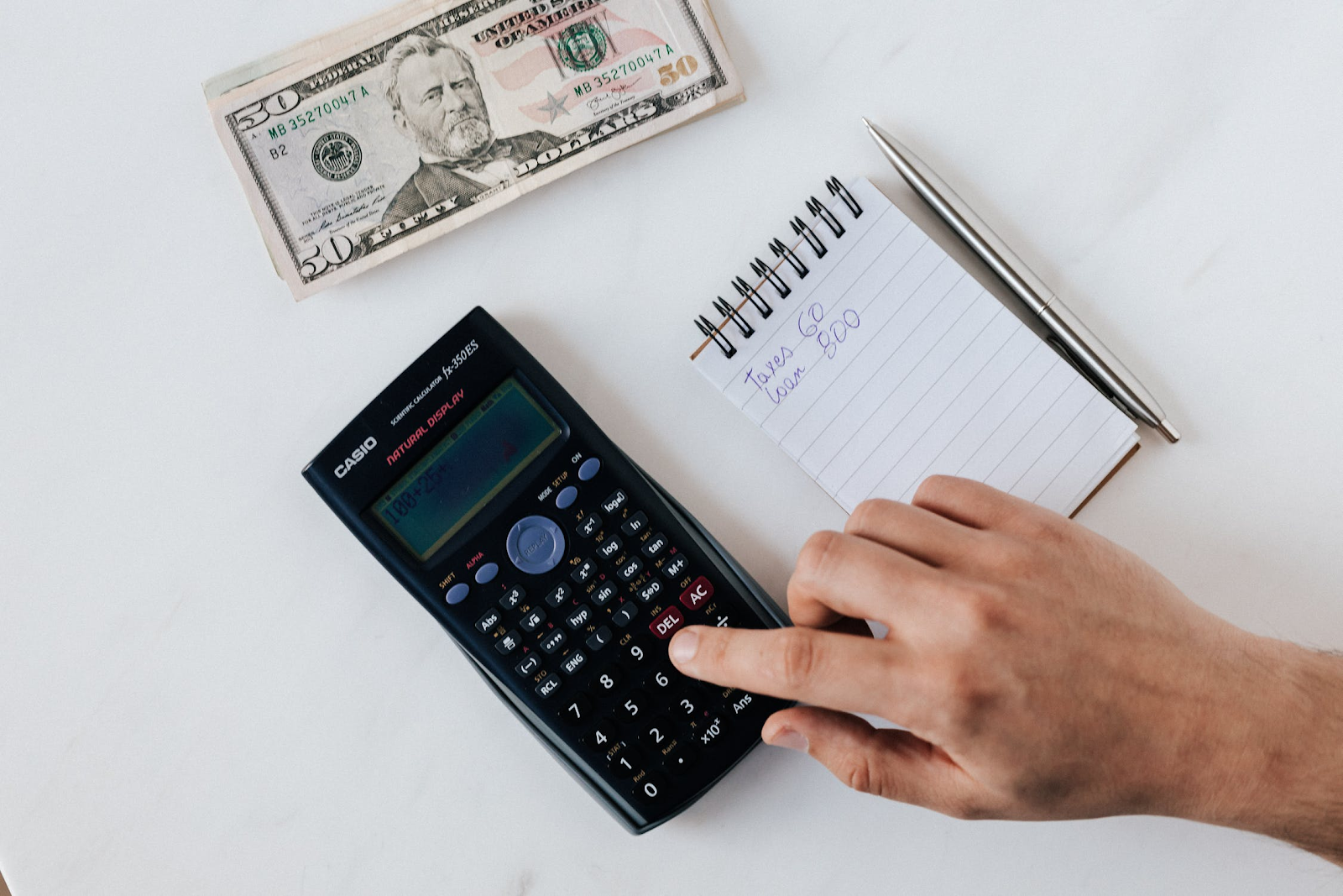 Accountant using a calculator to balance a budget with a notebook and a 50 US dollar banknote