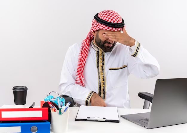 Tired UAE student in traditional wear, sitting with laptop, seeking resources and support.