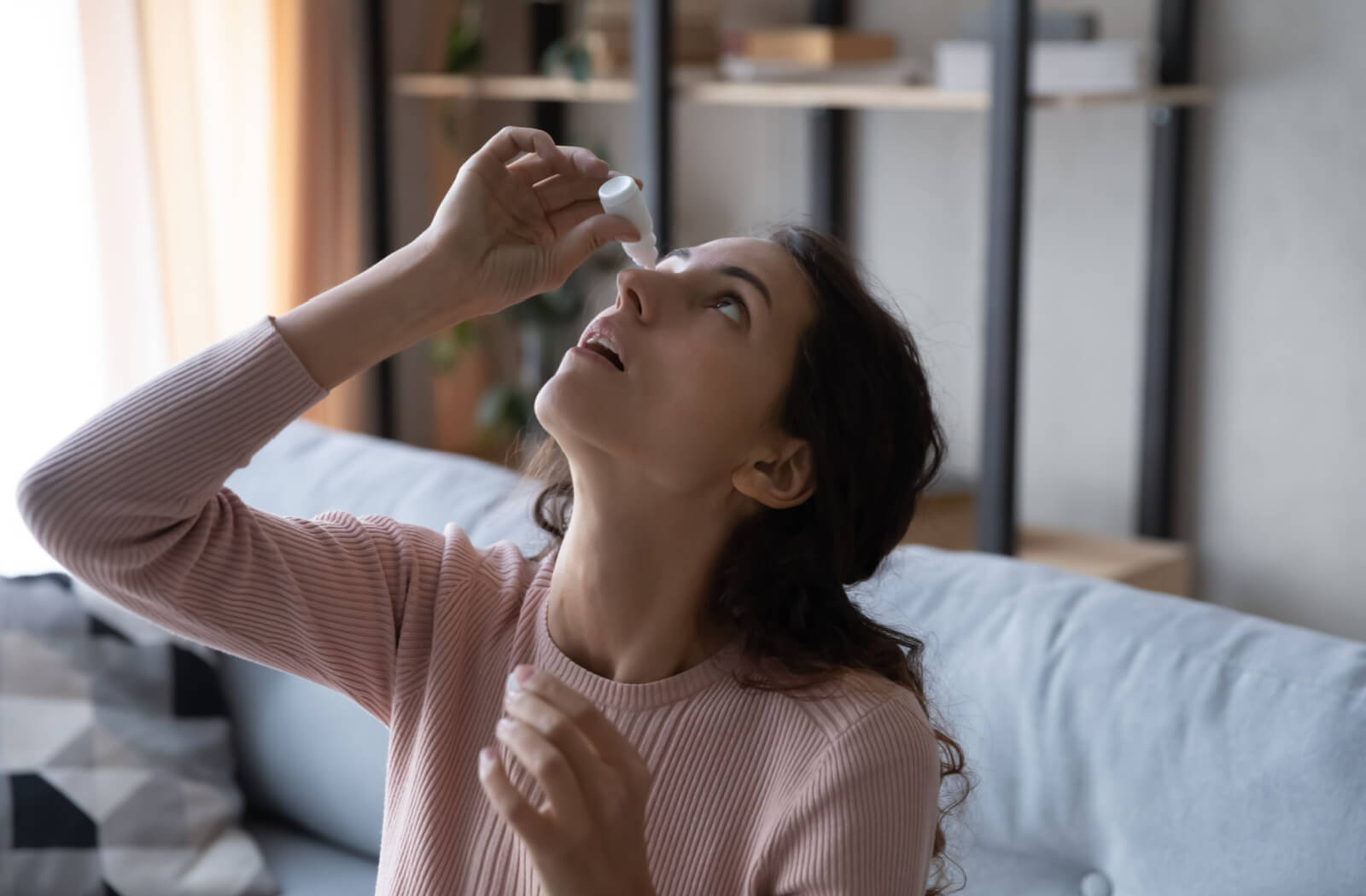 a woman applies restasis eye drops to treat dry eye