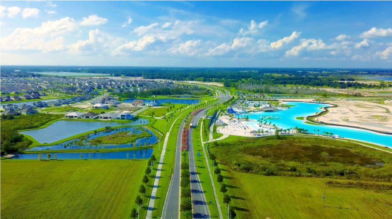 Aerial view of the Epperson master-planned community in Wesley Chapel, Florida. There are manicured green fields, rows of single-family homes, and a sandy lagoon for resident use just off the main road.