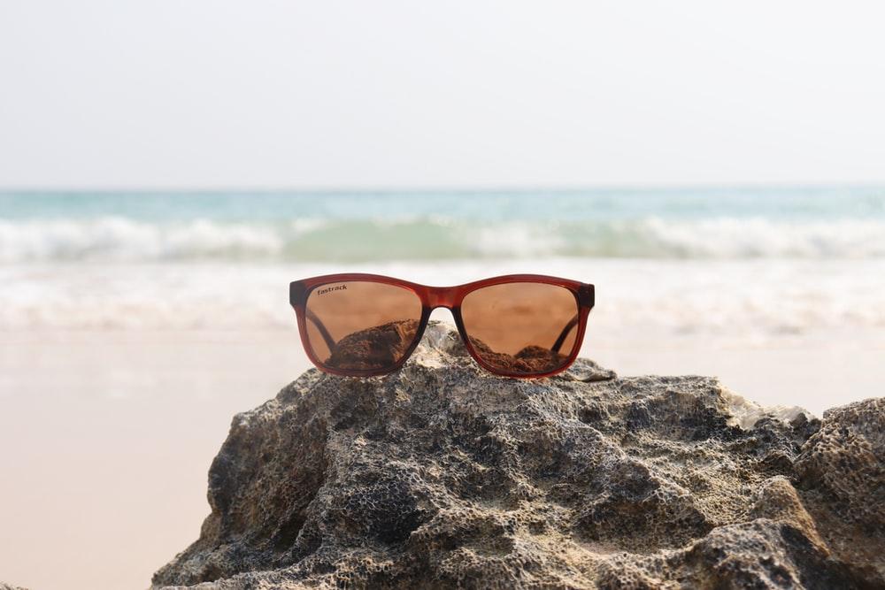 brown framed sunglasses on brown rock near sea during daytime