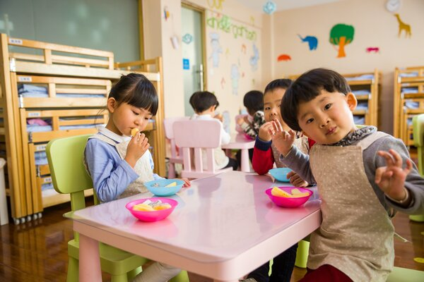 Preschool children seated across a table, enjoying snacks