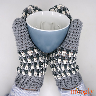 a pair of bulky black, white and gray mittens holding a cup