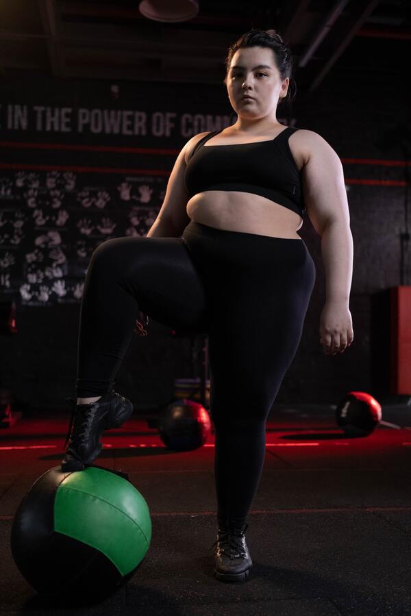 Foto de uma mulher plus size posando em uma academia com elementos para levantamento de pesos