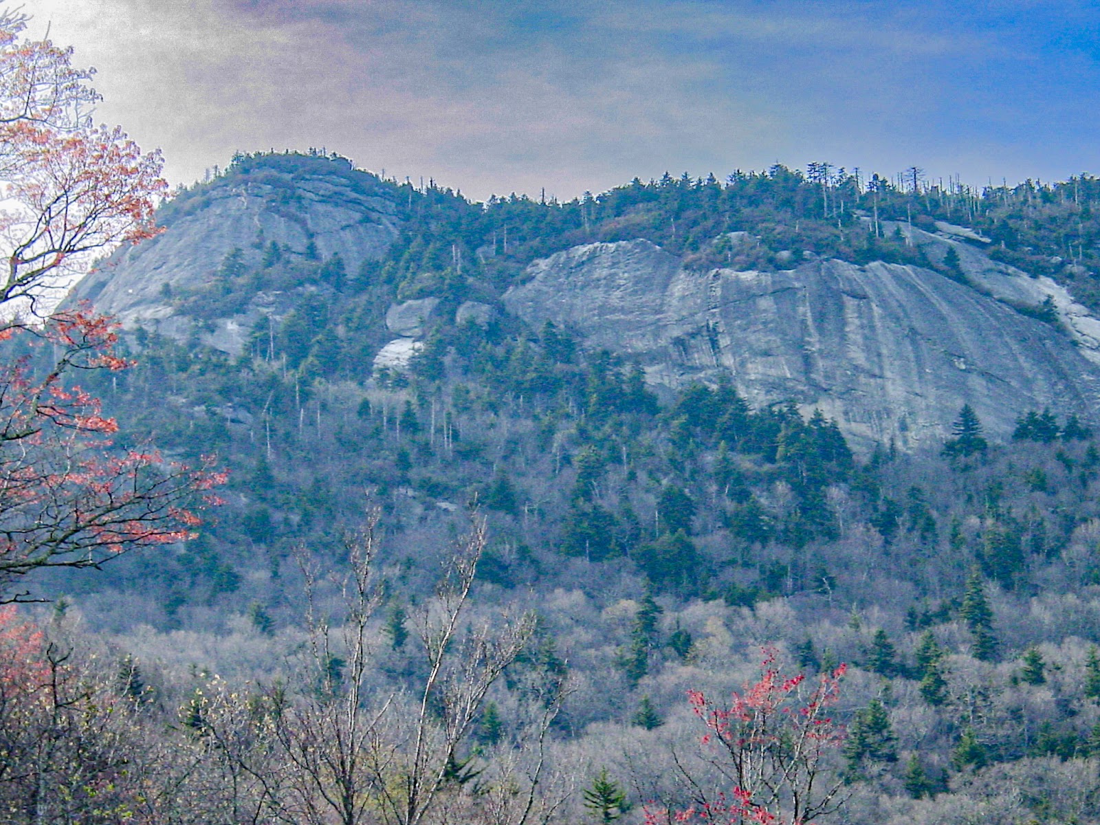 A large rocky cliff is surrounded by colorful trees and dramatic sky. 