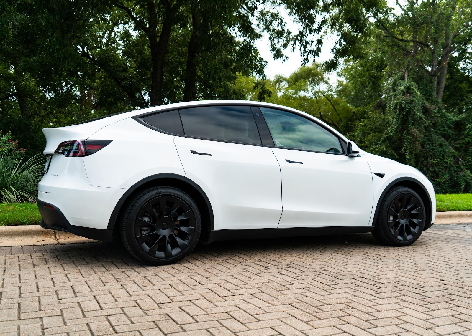 Tesla Model Y with white paint and blue wheels parked on cobblestone.