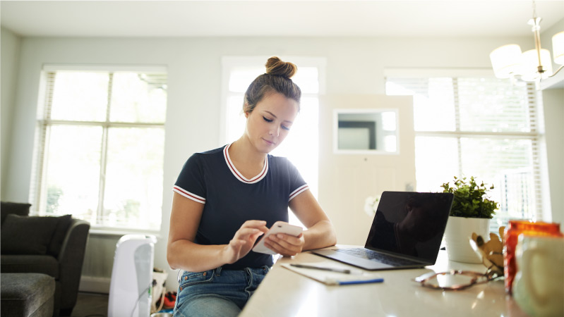 A young woman calculating her cost of living in Vancouver, BC, using her mobile phone and laptop.