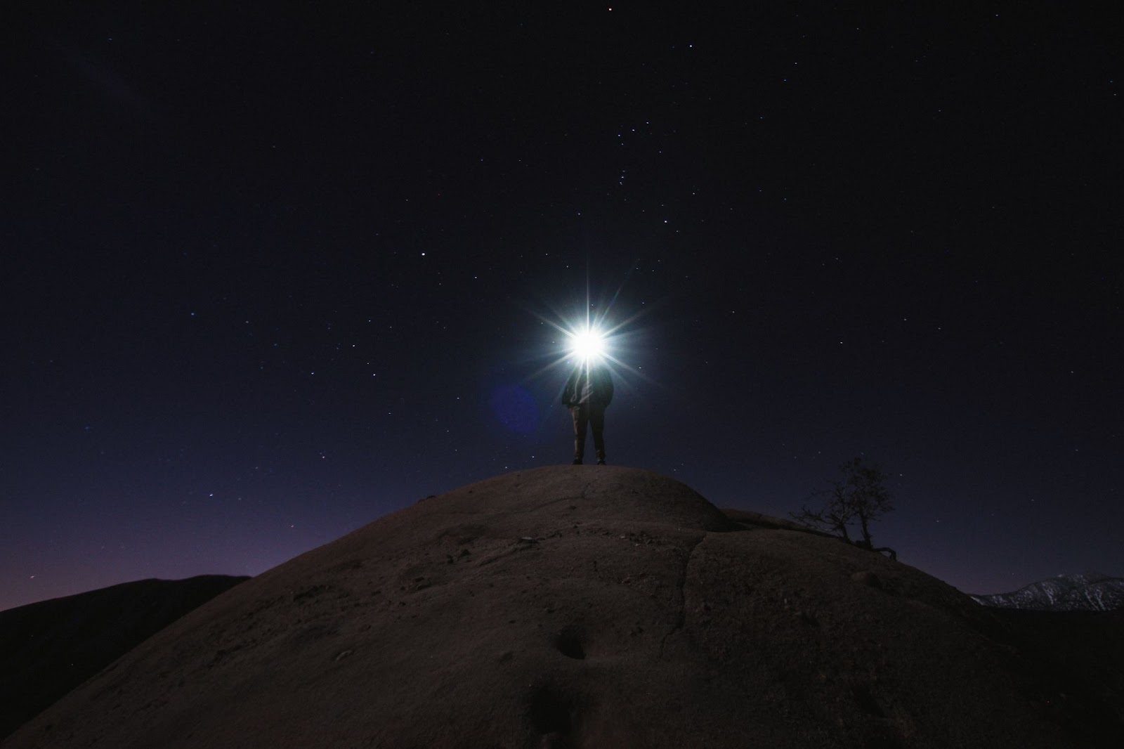 An silhouette of a man on a mountain at night, with a bright flash covering his face. 