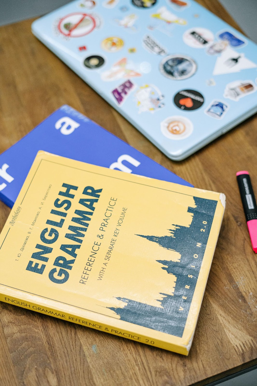 Some books and a laptop on a desk. The top book is called "English Grammar".