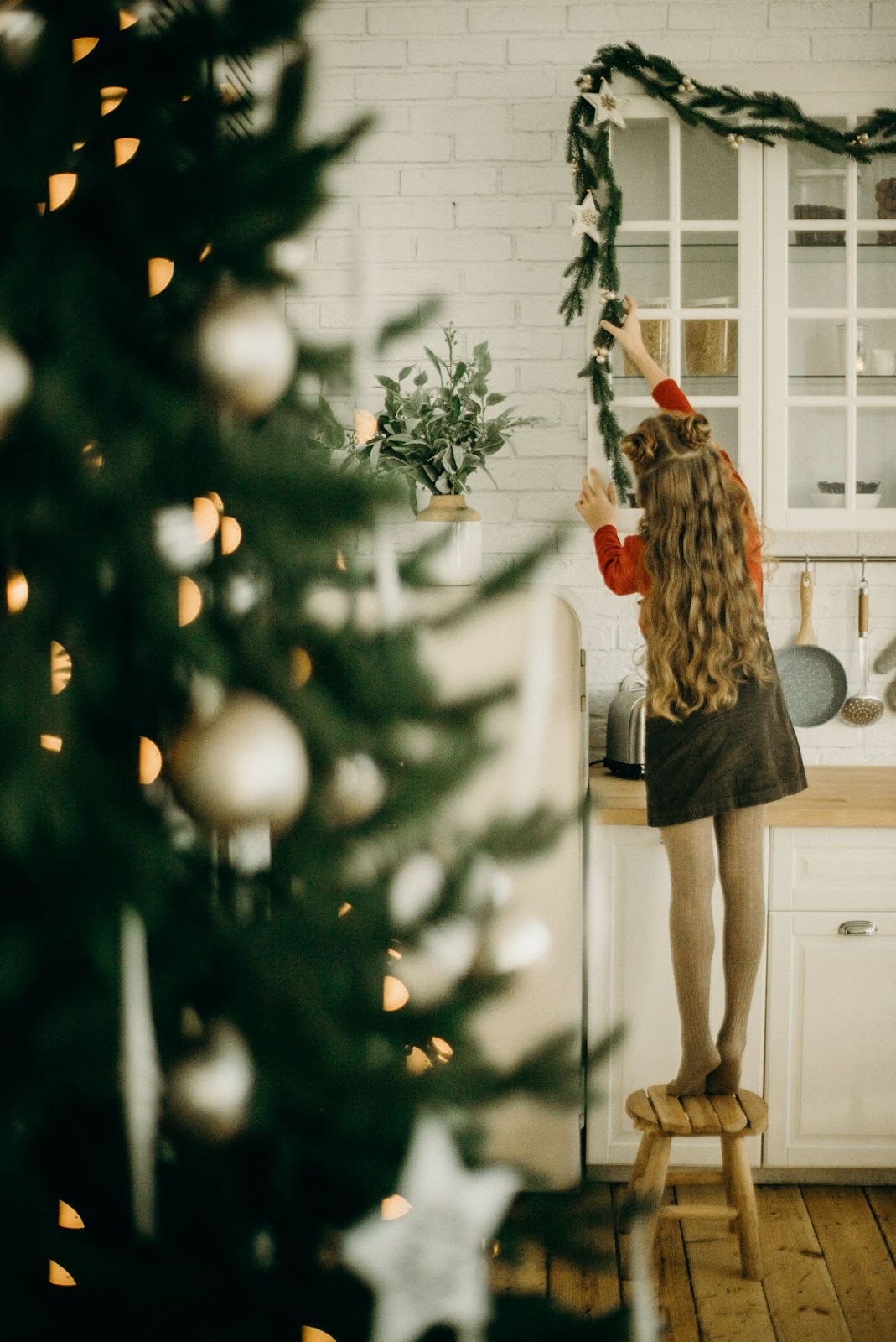 Young girl reaching for garland strung across kitchen cabinets.